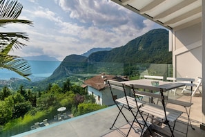 A balcony with a table and chairs overlooking a mountainous landscape. - Eco del Garda - XL Apartment 305 with Covered Terrace and Lake View (Tenno)