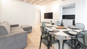 Een moderne woonkamer met een grijze bank, een eettafel gedekt voor vier personen, en een keuken met witte kasten en een zwart aanrecht.