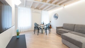 Een moderne woonkamer met een grijze bank, een eettafel met stoelen, een gitaar en een televisie aan de muur.