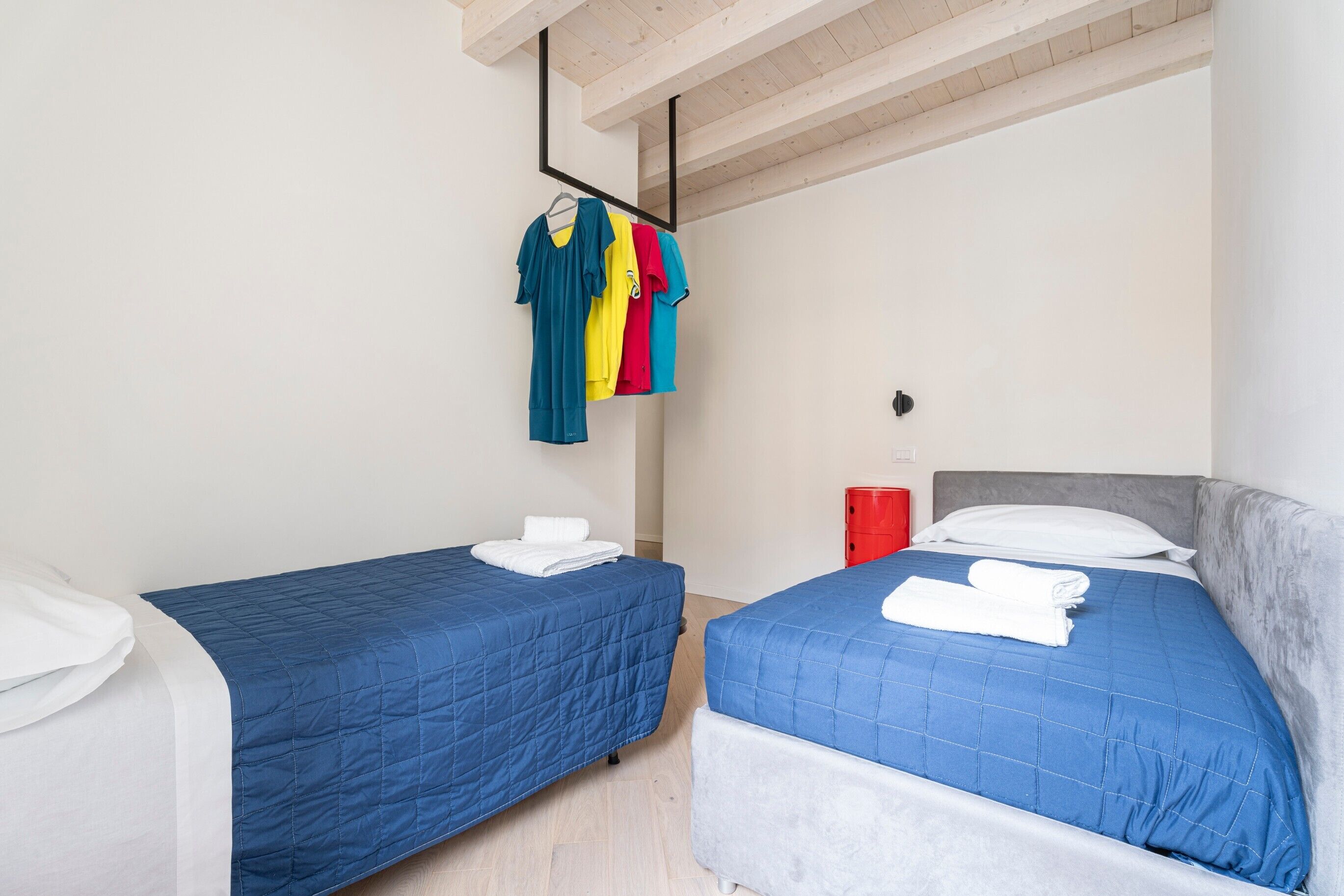 A room with two beds, each with a blue quilted bedspread and white pillows, and a wooden ceiling.