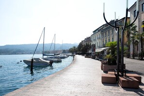 A waterfront promenade with boats docked, a row of buildings with balconies, and a clear sky.