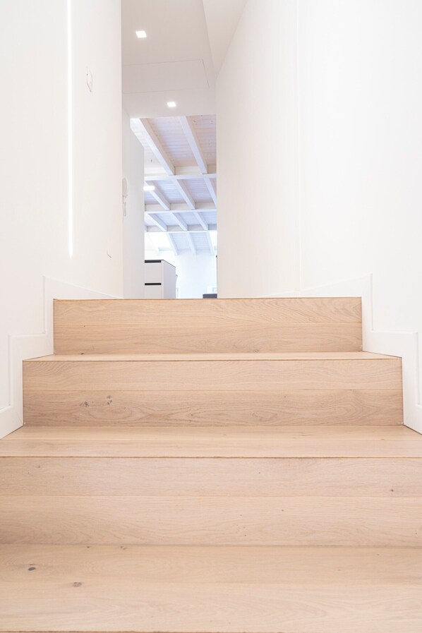 A staircase with wooden steps leading to a room with white walls and a ceiling with exposed beams.