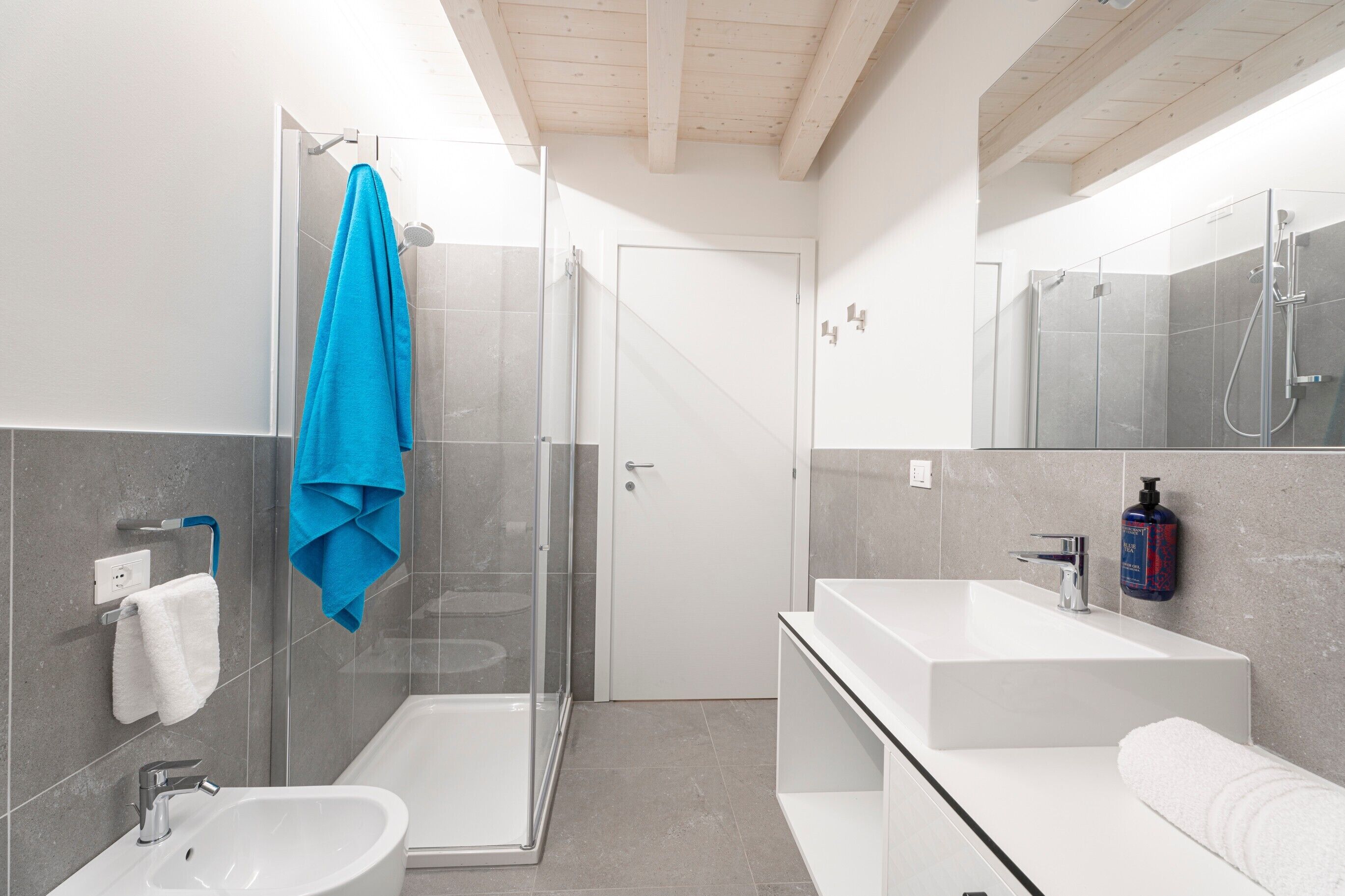 Une salle de bain moderne avec une douche à l’italienne en verre, un lavabo blanc et un grand miroir.