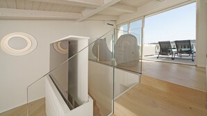 Een modern interieur met een glazen trap, houten vloeren en uitzicht op een terras.