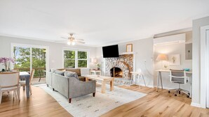 A modern living room with a stone fireplace, a sofa, a dining table, and a TV. - Mountain Retreat, Balcony, Grill, and 5 Minutes to Downtown! (Blowing Rock)