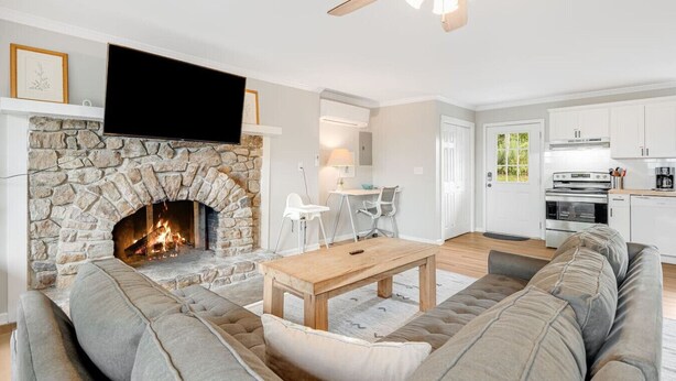 A living room with a stone fireplace, a flat-screen TV, a sofa, a coffee table, and a ceiling fan. - Mountain Retreat, Balcony, Grill, and 5 Minutes to Downtown! (Blowing Rock)