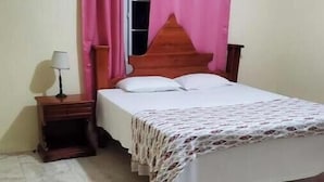 A bedroom with a bed, a nightstand, a lamp, and a window with pink curtains. - Pvalley Suite 10B 1 Bedroom (Hatfield)