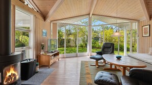 Ein gemütliches Wohnzimmer mit Kamin, bequemen Sitzmöglichkeiten, einem Esstisch und großen Fenstern mit Blick auf den Garten.