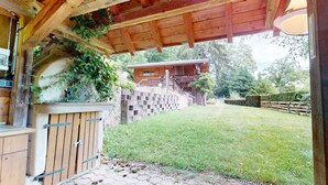 En stuga byggd av trä med en inglasad veranda, en mur av tegelsten och en gräsklädd trädgård.