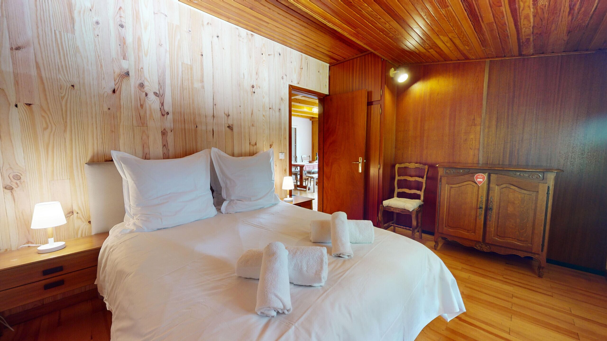 A wooden-paneled bedroom with a bed, nightstands, a chair, and a wardrobe.