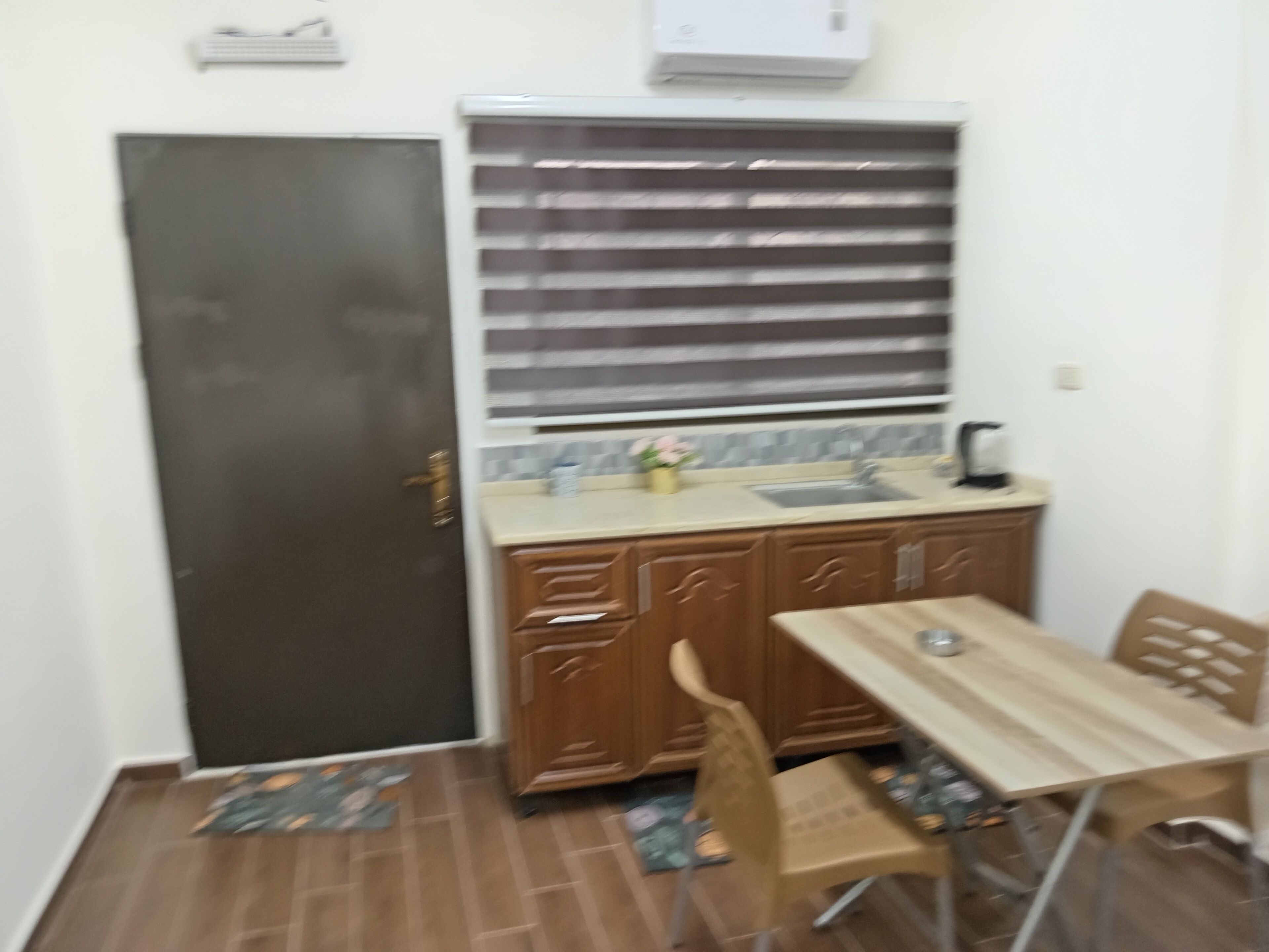 A small kitchen with a sink, cabinets, and a window with blinds.