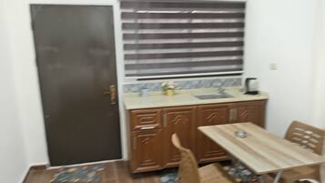 A small kitchen with a sink, cabinets, and a window with blinds.
