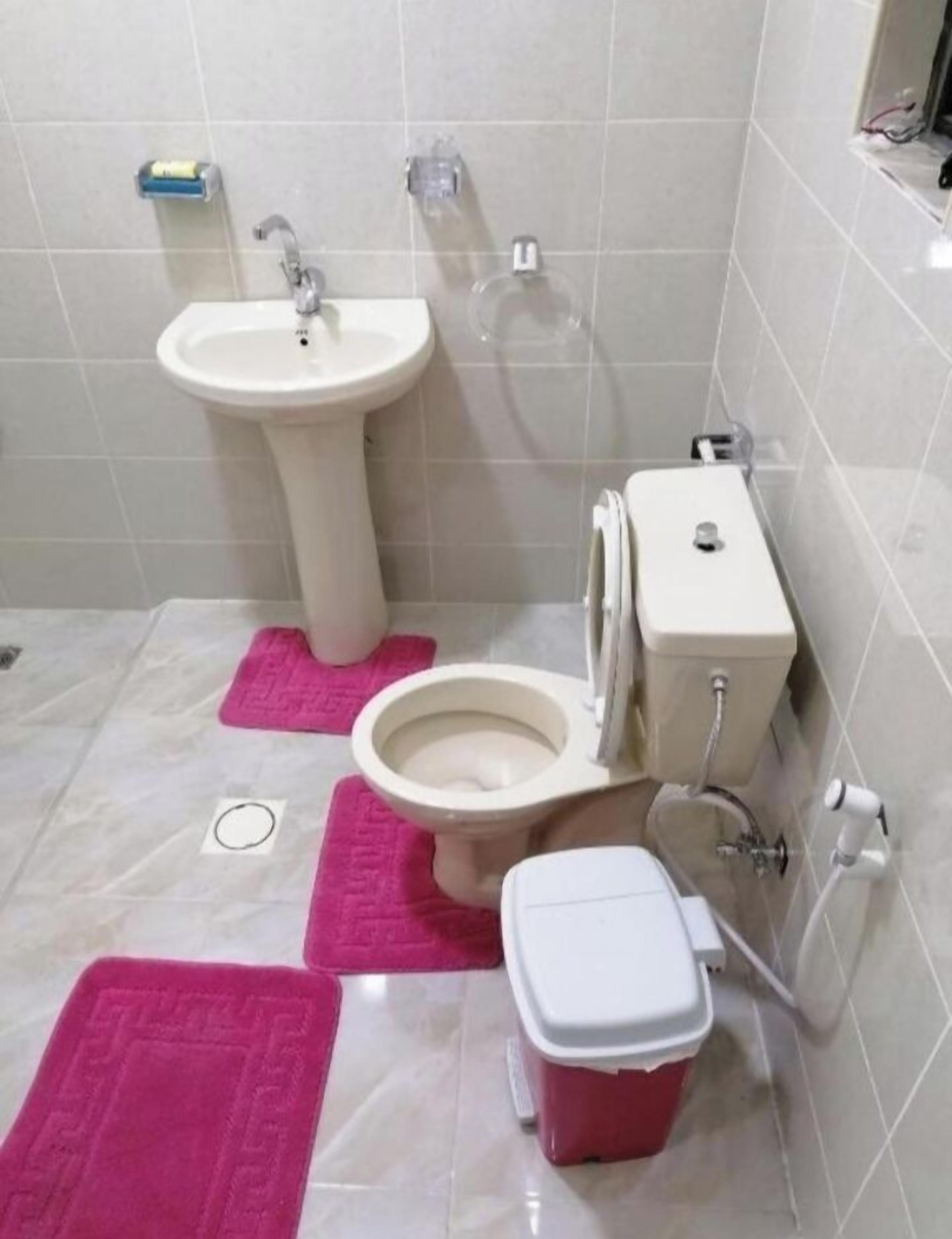 Un baño con lavamanos pedestal, inodoro, bidé y un cubo de basura rojo.
