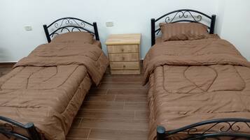 Habitación doble con dos camas, una mesita de noche de madera y una pared blanca lisa.