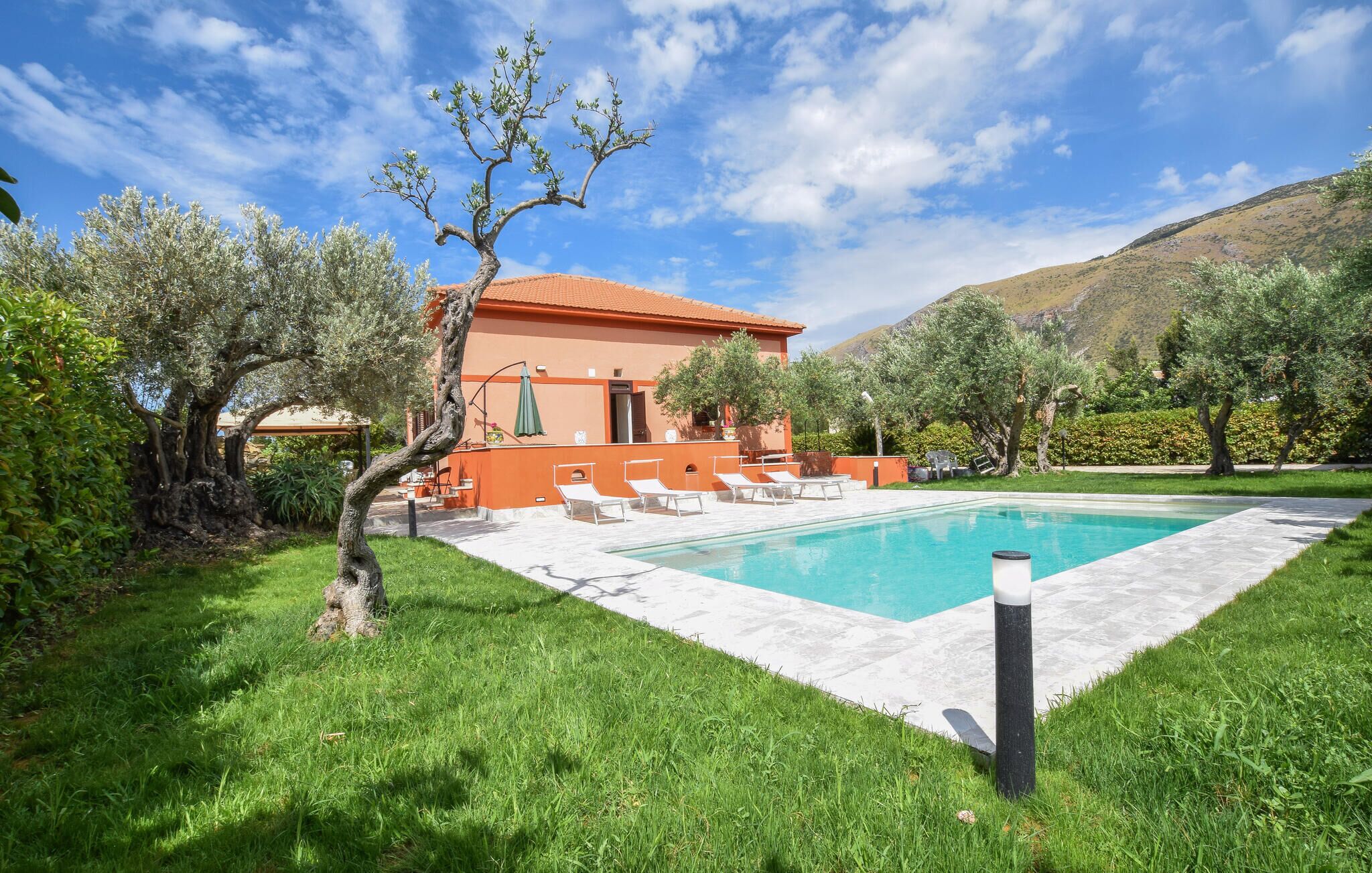 A villa with a swimming pool, outdoor seating, and a mountain backdrop.