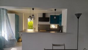A modern kitchen with a central island, pendant lights, and teal cabinets. - Gîte ô Naturel - nature and comfort getaway (Buzancy)