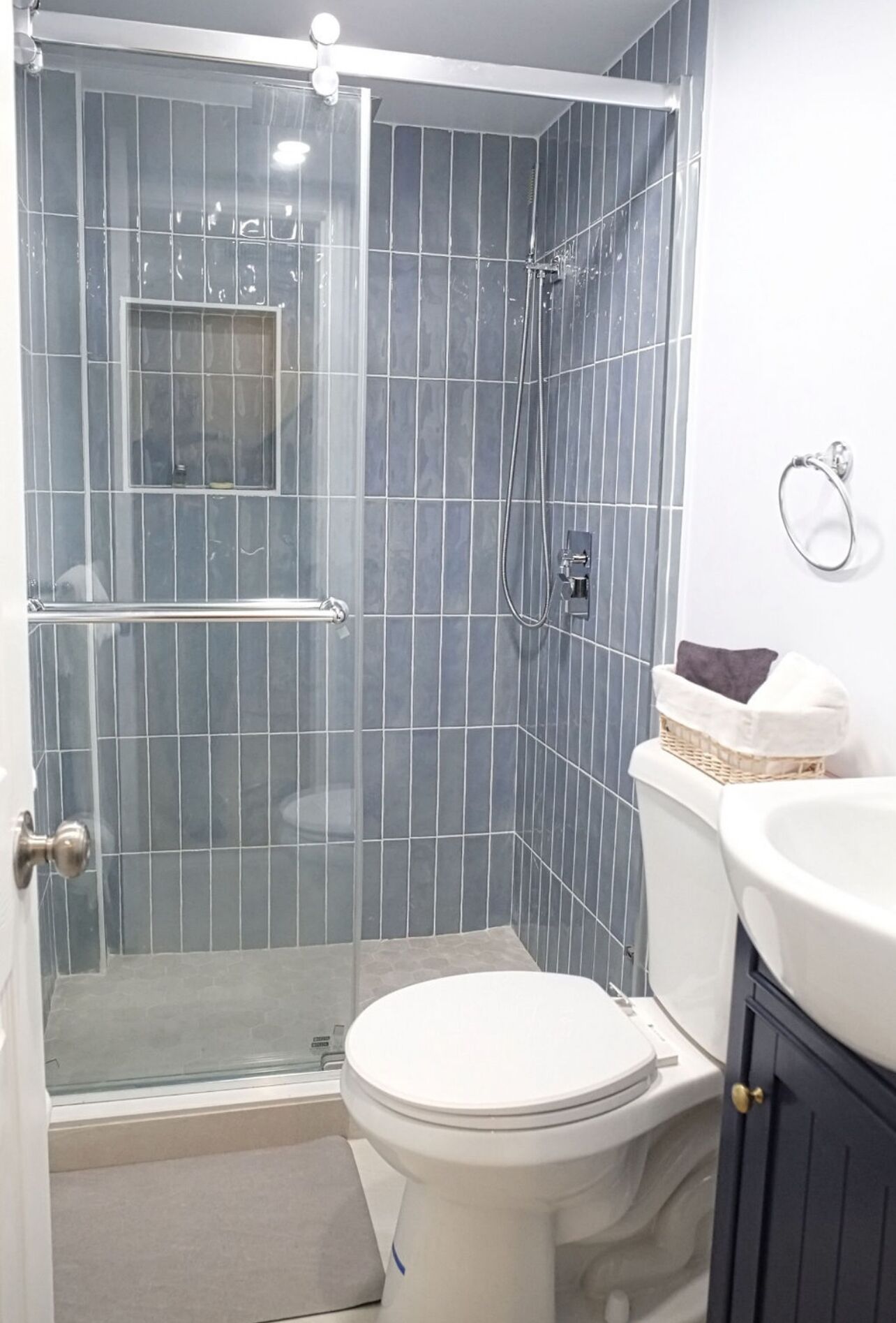 A bathroom with a glass-enclosed shower, a white toilet, and a sink with a basket of towels.