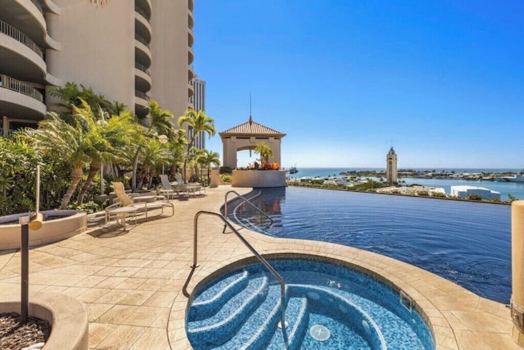 A hotel pool area with a hot tub, lounge chairs, and a view of the ocean.
