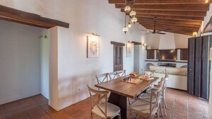 A dining area with a wooden table and chairs, a kitchen in the background, and a ceiling fan. - Finca Mojito Cómpeta by Ruralidays (Málaga)