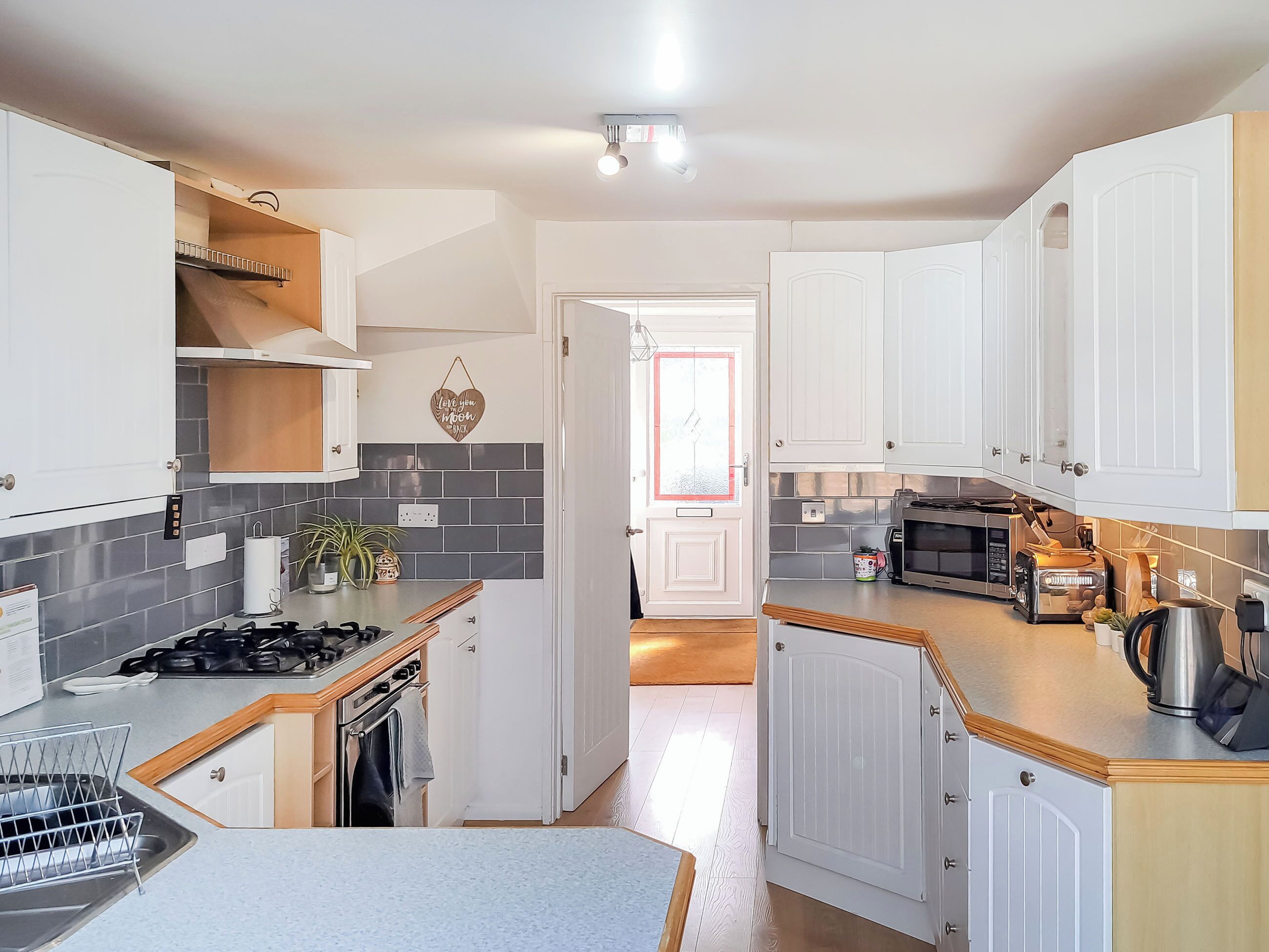 A modern kitchen with white cabinets, a built-in oven, a microwave, and a kettle.
