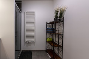 Une pièce avec une porte vitrée, un radiateur blanc et une étagère en métal où sont pliés des vêtements.