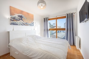 Une chambre à coucher avec un lit, un tableau, une télévision et une fenêtre avec des rideaux.