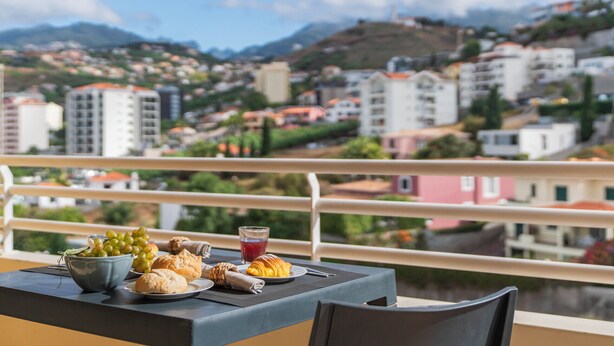 Un balcon avec une table préparée pour le petit-déjeuner, donnant sur une ville située sur une colline.