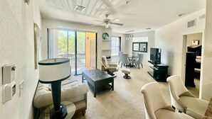Ein geräumiges Wohnzimmer mit Deckenventilator, einer Couch, einem Couchtisch und einem Fernseher.
