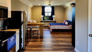 A compact kitchen with modern appliances, a dining area with a wooden table and chairs, a small TV, and a cozy bed with a striped bedspread. - New for 2026. Private driveway and new private entrance. (Mystic)