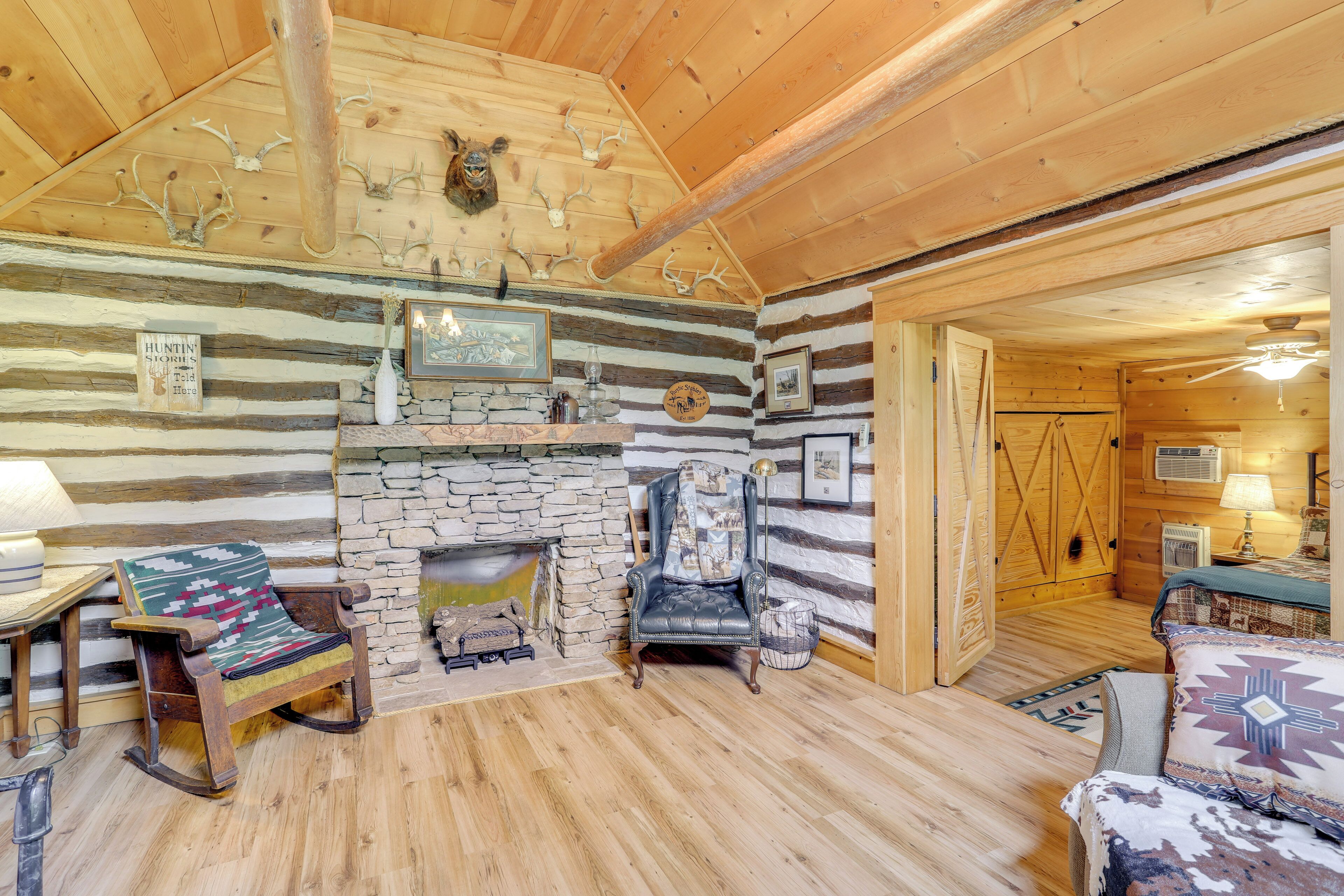 A log cabin interior with a stone fireplace, wooden walls, and antler decorations.