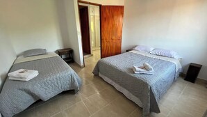 A hotel room with two beds, each with a grey quilt and pillows, and a wooden door leading to another room.