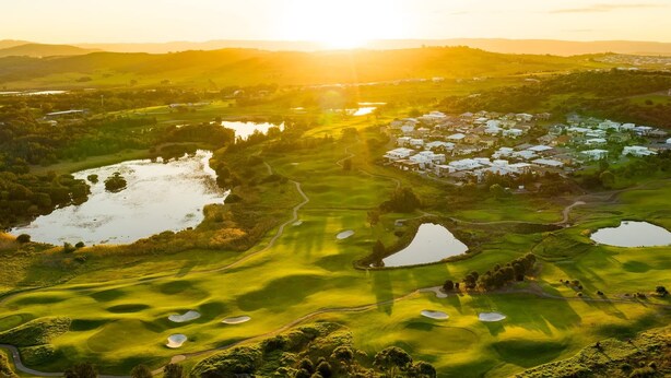 Ein Golfplatz mit Bunkern, Wasserhindernissen und einer Wohngegend im Hintergrund.