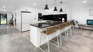 Cozinha moderna com armários brancos, bancada preta e uma ilha central com banquetas.