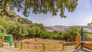 Vista panorámica desde un balcón con un camino de grava, baranda de madera y un cubo de basura verde.