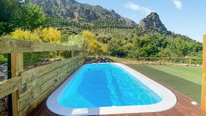 Un jacuzzi rectangular con una terraza y valla de madera, rodeado de vegetación exuberante y montañas al fondo.