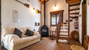 Una sala de estar acogedora con un sofá color beige, una estufa de leña, una escalera y una silla de madera.