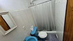 Un baño pequeño con paredes de azulejos blancos, un inodoro azul, un bidé azul y una cortina de ducha.