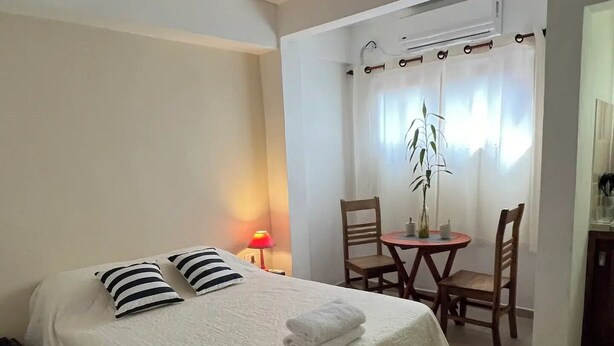 Una habitación de hotel con cama, escritorio, silla, lámpara y ventana con cortinas.