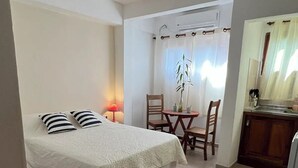 Una habitación de hotel con cama, una mesita con sillas, una lámpara en el techo y un ventanal con cortinas.