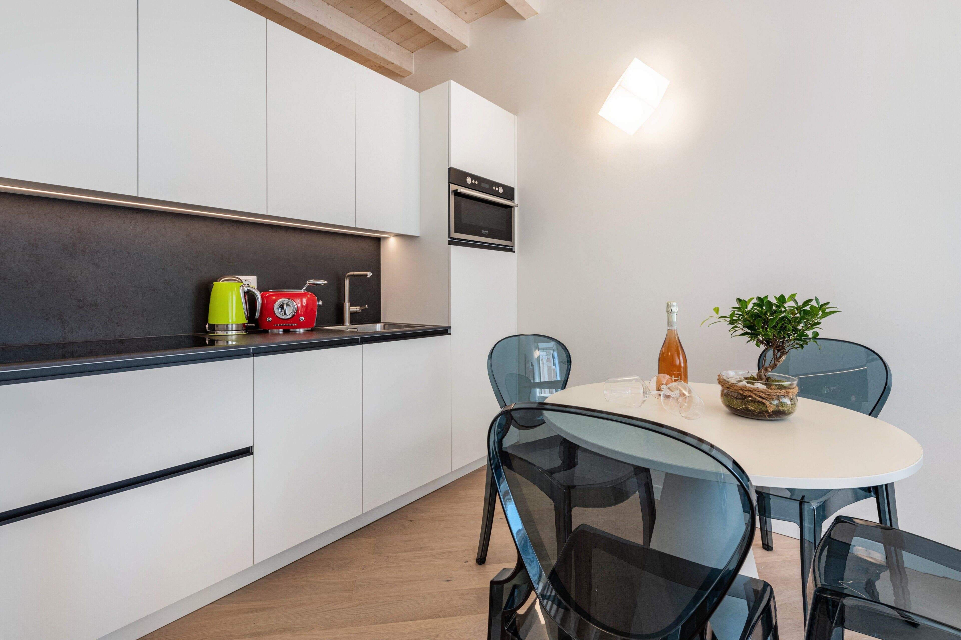 Una cucina moderna con mobili bianchi, forno integrato e zona pranzo con tavolo e sedie in vetro.