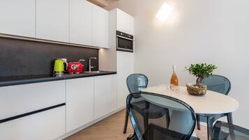Una cucina moderna con mobili bianchi, forno integrato e zona pranzo con tavolo e sedie in vetro.