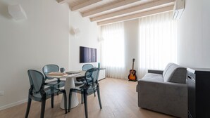 A modern living room with a dining area, a grey sofa, a guitar, and a flat-screen TV on the wall. - Apartment 'Flat 3' with Lake View, Wi-Fi and Air Conditioning (Salò)