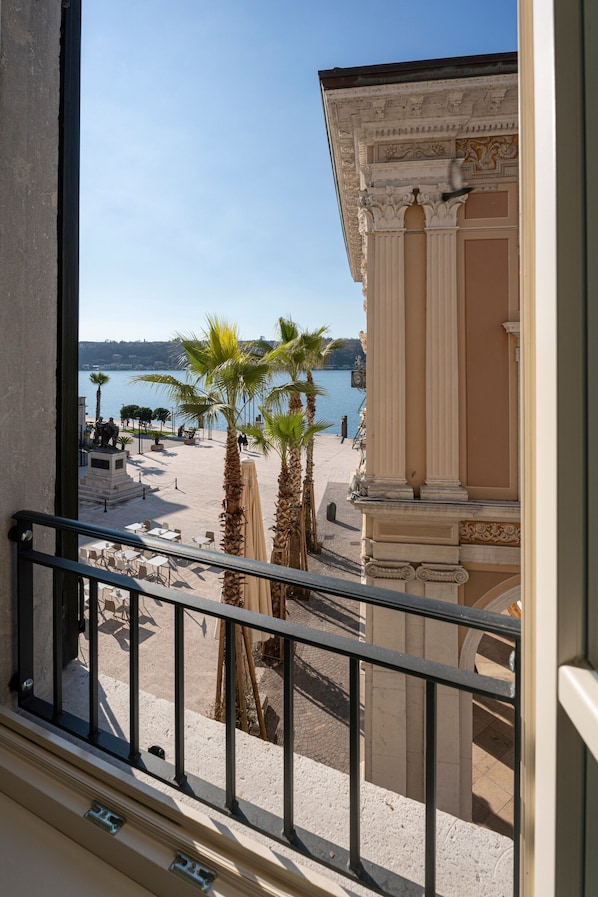 A balcony with a view of a beach, palm trees, and a building with classical architecture.