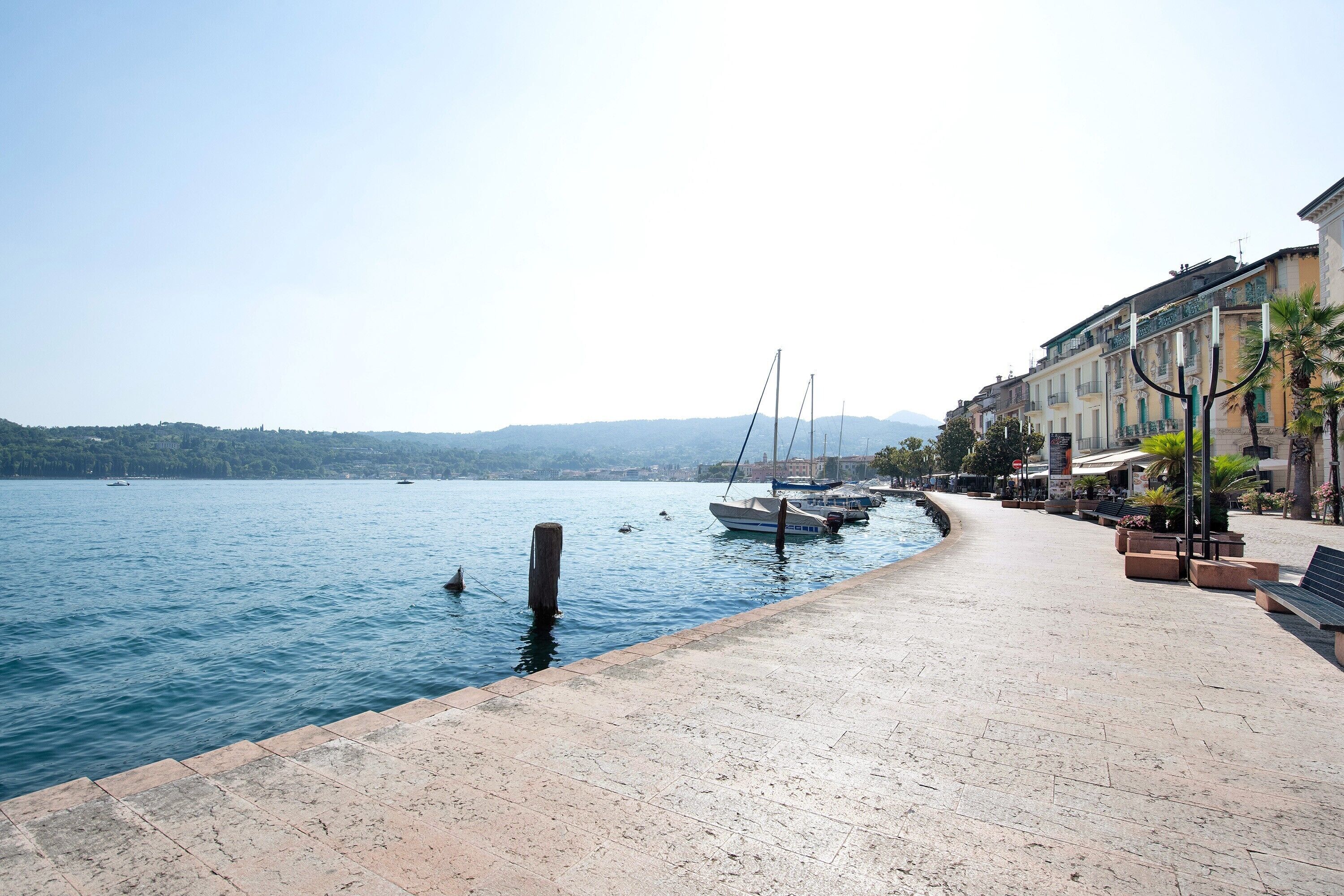 Une promenade en bord de mer, avec des bateaux amarrés, un sentier pavé et des bâtiments dotés de balcons.