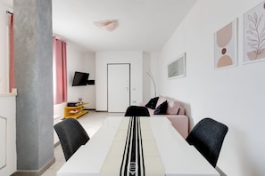 Una sala de estar moderna con un sofá blanco, una mesa de comedor y un televisor en la pared.