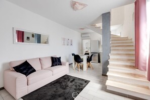 A modern living room with a pink sofa, a black rug, and a staircase leading to another level. - Dimora Cadeddu (Oristano)