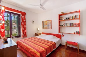 Une chambre à coucher comprenant un lit, une bibliothèque, un bureau, une chaise, une fenêtre avec des rideaux, un ventilateur de plafond et une étagère fixée au mur.