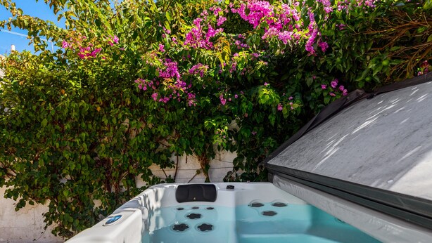 A hot tub with a clear view of the water jets, surrounded by lush green foliage and pink flowers. - Holiday Home 'Alojamento Local Coruche Erra' with Lake View, Wi-Fi and Air Conditioning (Coruche)
