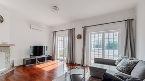 A living room with a TV, sofa, and a glass coffee table. - Holiday Home 'Alojamento Local Coruche Erra' with Lake View, Wi-Fi and Air Conditioning (Coruche)