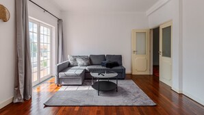 A modern living room with a grey sofa, a round coffee table, and a large window with curtains. - Holiday Home 'Alojamento Local Coruche Erra' with Lake View, Wi-Fi and Air Conditioning (Coruche)